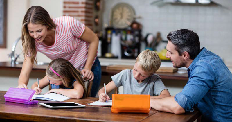 mother and father helping children with homework at kitchen table