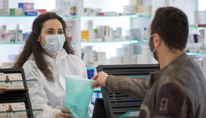 pharmacist wearing a msak hands bag to a customer