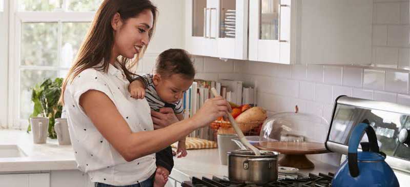 mother holding baby and cooking on stove
