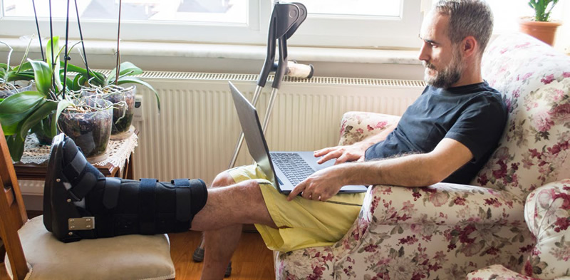 man sitting on couch with a broken leg using a laptop computer