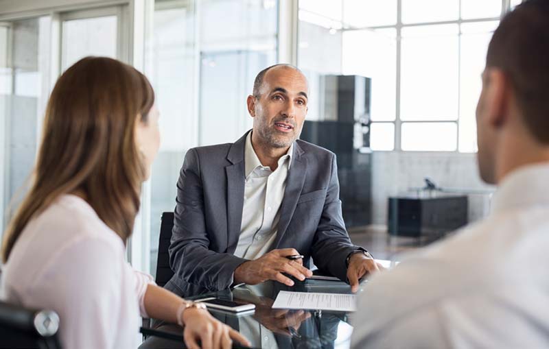 man in business attire talking with two people in a conference room