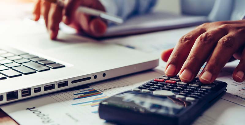 pair of hands working on laptop and calculator