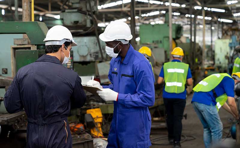 masked workers writing on a clipboard in a factory