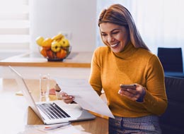 woman uses phone and laptop to work on paperwork