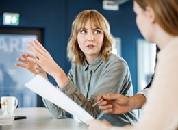 two women holding paper and talking