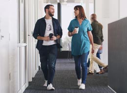 two employees walking, talking and holding coffee