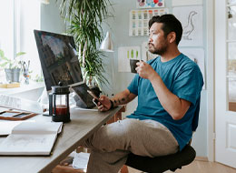 man drinking coffee holding cellphone and looking at laptop