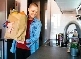 woman carrying a paper bag of groceries into kitchen