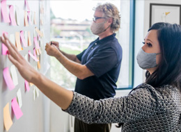 two masked employees putting sticky notes on wall