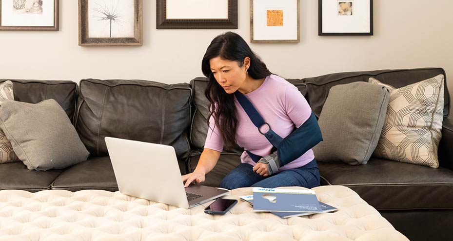 woman with broken arm sitting on the couch looking at laptop