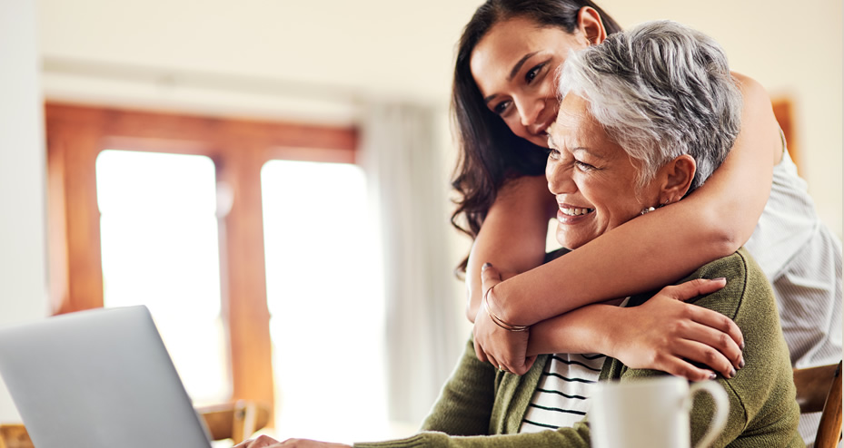 mother and daughter hugging while looking at laptop