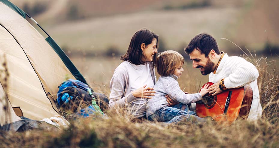 family playing guitar outside of camping tent