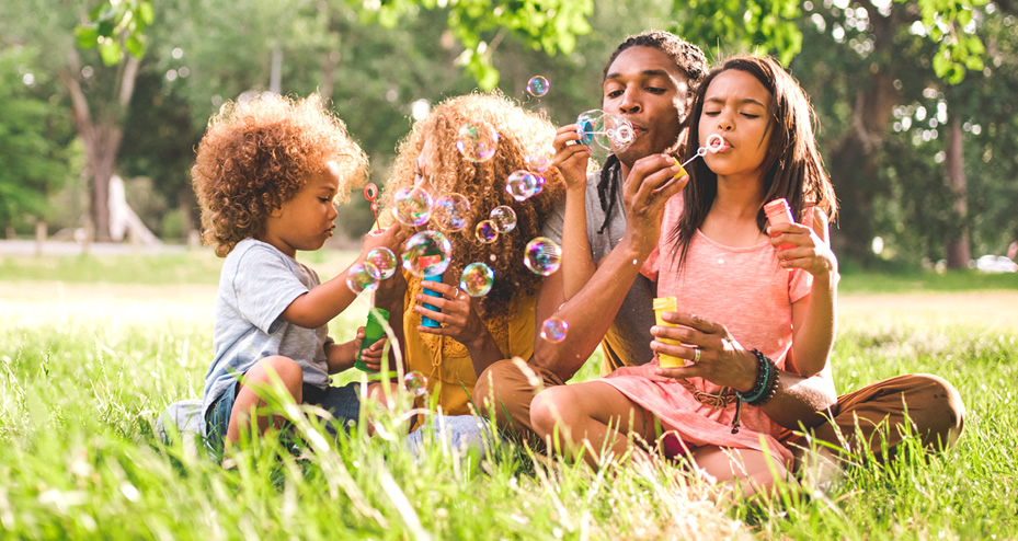 family sitting in park blowing bubbles