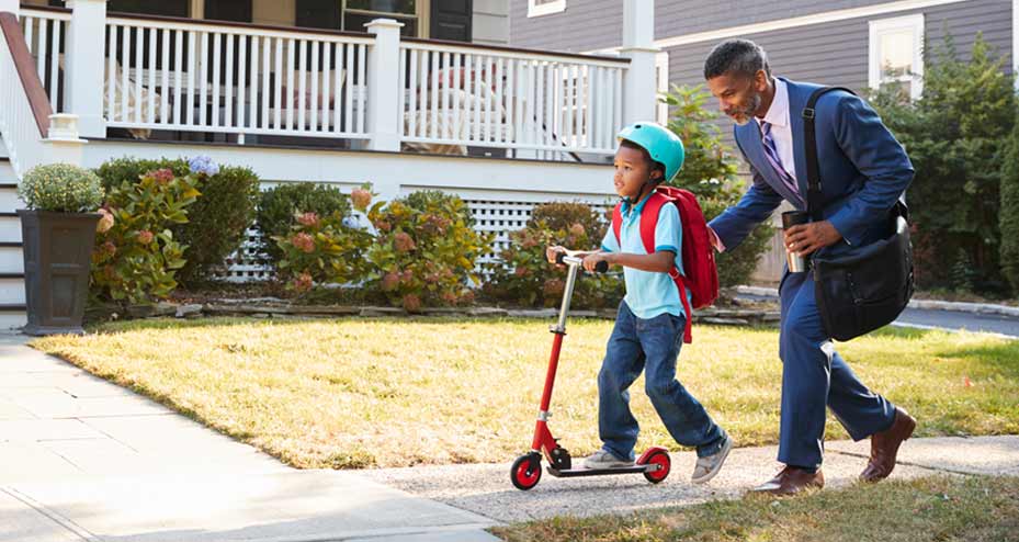 father dressed for work walking next to son on scooter